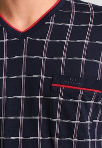 Marineblauwe V-hals shirt met rode accenten, voorzien van een gridpatroon in wit en rood, en een borstzak met contrasterende rand en logodetail.