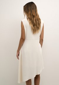 Vestido marfil con un dobladillo asimétrico, mangas cortas y tejido suave, que presenta un diseño de espalda sin costuras y sutiles detalles drapeados.