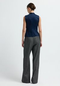 Blusa senza maniche blu navy con una texture liscia, abbinata a pantaloni grigi a vita alta con un motivo scintillante. Tutti i capi hanno una vestibilità su misura.