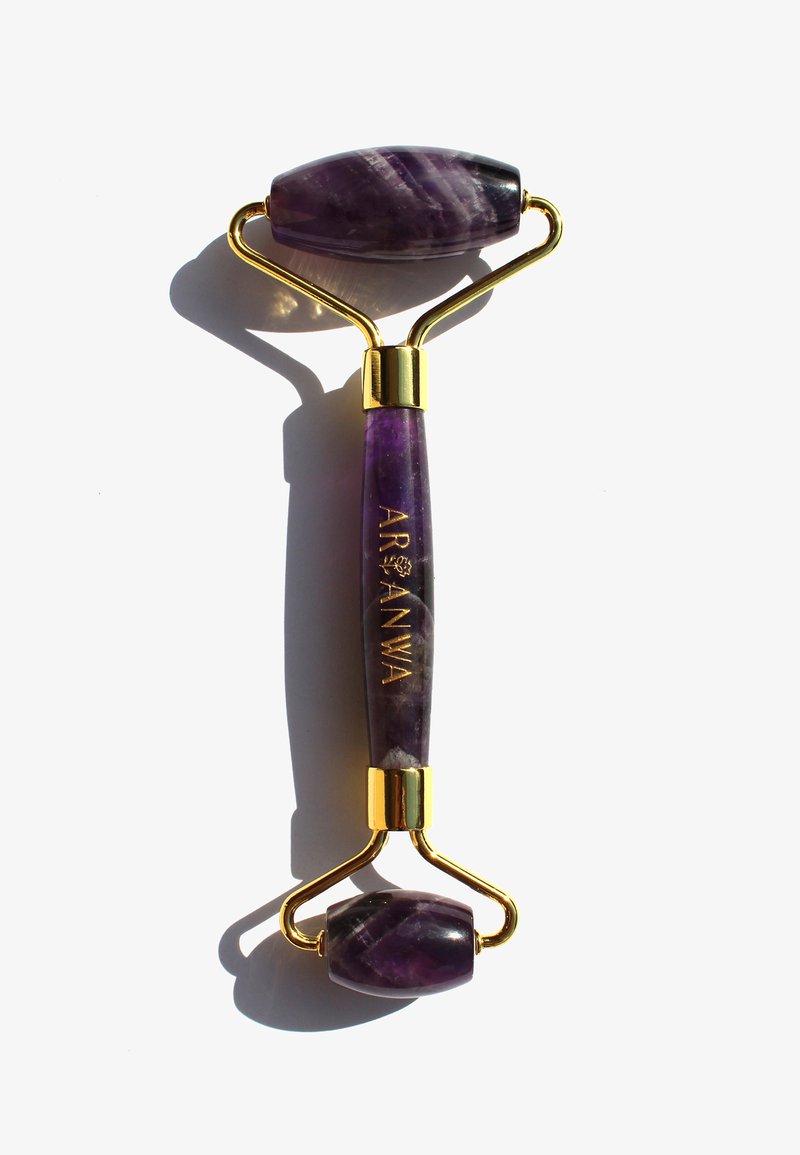 Purple amethyst facial roller with a gold frame, featuring an oval and rounded end, smooth texture, and engraved logo on the handle.