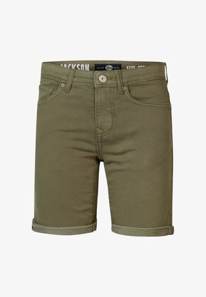 Boy wearing pale yellow polo shirt, olive rolled-up shorts, white socks, and white sneakers standing against plain background.