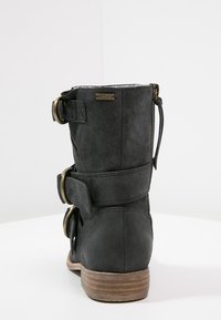 Černé kotníkové boty s semišovým povrchem, vybavené dvěma velkými kovovými sponami, bočním zipem a hnědým dřevěným podpatkem. Logo připevněné na zadní straně.