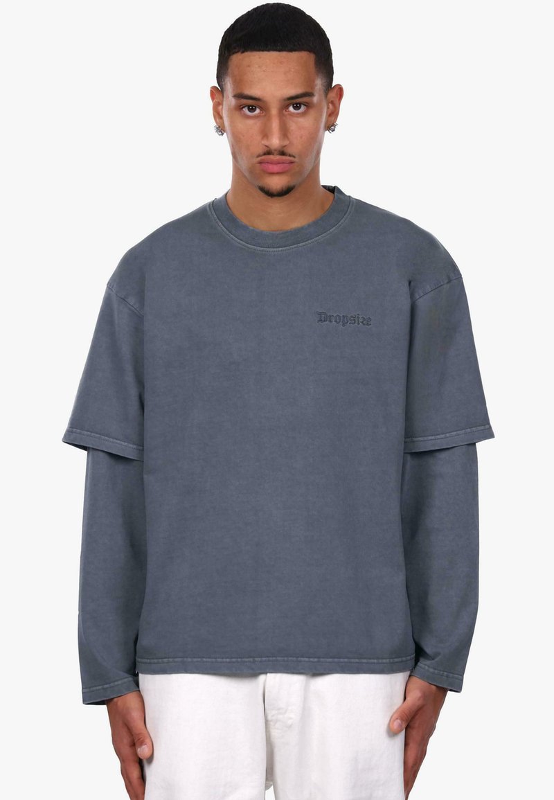 Szara, oversize bluza z okrągłym dekoltem, warstwowymi krótkimi rękawami oraz haftowanym logo "Dropsize" na piersi. Wykonana z bawełny, o miękkiej fakturze.