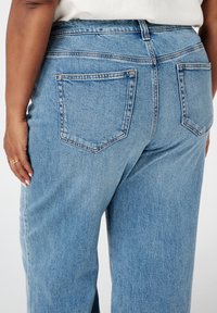 Lichtblauwe denim jeans met een relaxte pasvorm, voorzien van dubbele achterzakken en zichtbare stikdetails. Zachte textuur met een casual ontwerp.