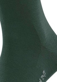 Zielona, dziana skarpetka z prążkowanym wzorem i wzmocnionym palcem, z białym logo w pobliżu kostki. Kształt zaprojektowany dla komfortu i dopasowania.