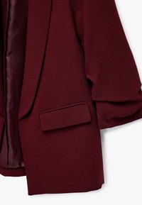 Burgundy blazer med en glat tekstur, der har en enkelt brystlomme, brede ærmer og en satinforing indvendig.