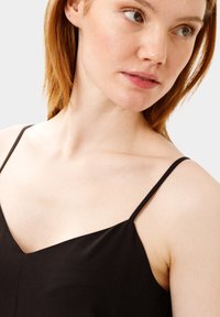 Sort camisole med tynde stropper, V-udskæring, glat tekstur og let løst fit, med en klassisk silhuet og minimalistisk design.