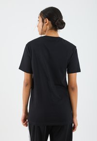 T-shirt en coton noir, à manches courtes, coupe décontractée. Texture lisse avec un col rond, affichant un design minimaliste sans logos ni motifs visibles.