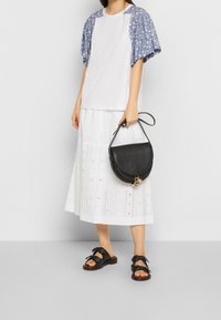 Top blanco con mangas abullonadas de flores azules, falda blanca de volantes con detalles recortados, bolso cruzado negro y sandalias negras con lazos.