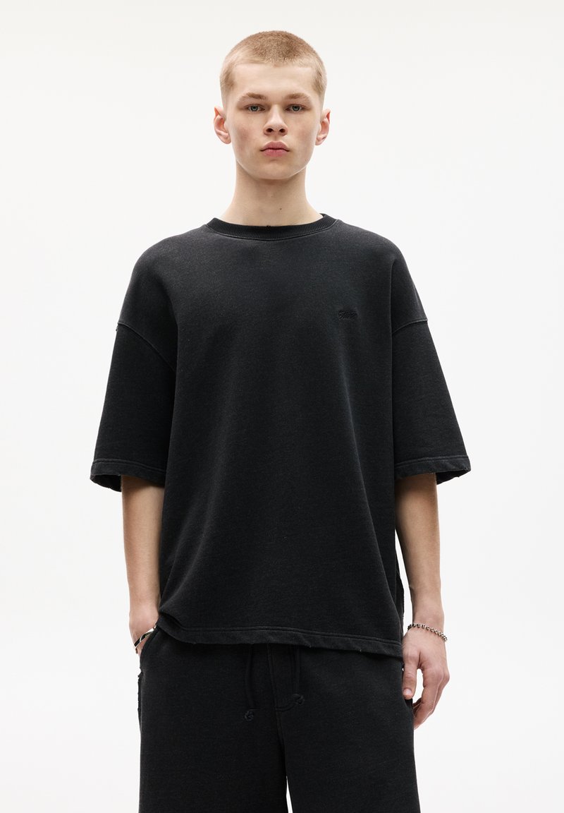 Černé oversized tričko vyrobené z bavlny, s krátkými rukávy a žebrovaným kulatým výstřihem. Jednoduchý design s jemným logem.