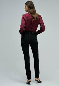 Blusa de satén granate con mangas largas, combinada con jeans negros ajustados. Zapatos de tacón negro completan el look. Texturas suaves evidentes.
