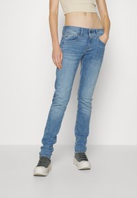 Jeans azzurri chiari con vestibilità slim, dotati di cinque tasche e chiusura con bottone. Indossati con un crop top beige e sneakers piattaforma grigie.