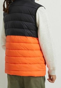 Kamizelka pikowana z czarną górną częścią i jaskrawo pomarańczowym dołem. Posiada poziomą pikowaną strukturę i bezrękawnikowy fason.