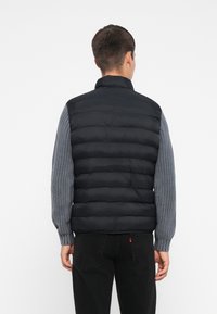 Melns pūšamais vestes ar augstu apkakli, kuram ir ērti adīti pelēki piedurknes. Dizains ietver horizontālas šuves un rāvējslēdzēju.