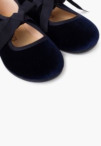 Zapatos de ballet de terciopelo azul marino con punta redondeada, cintas elásticas de raso azul marino y un forro interior suave. Presenta una suela plana negra.