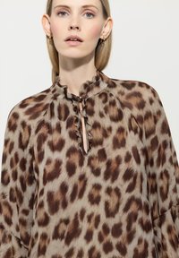 Leopardenmuster-Bluse in Hellbraun und Beige, mit einem Rüschkragen und einem Schlüsselloch-Ausschnitt. Weicher, fließender Stoff.
