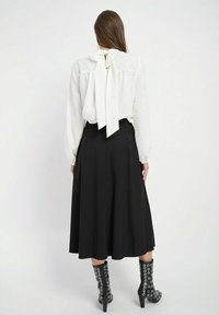 Biała bluzka z wiązaniem przy szyi, w fakturze w kropki; zestawiona z czarną, zwiewną spódnicą i czarnymi botkami do kolan z srebrnymi oczkami.