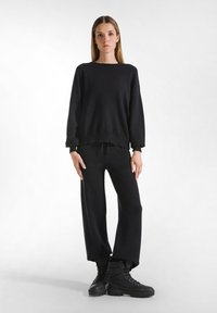 Maglione nero a maglia con scollo rotondo e vestibilità rilassata, abbinato a pantaloni neri a gamba larga e stivali neri con lacci. Texture liscia in tutto.