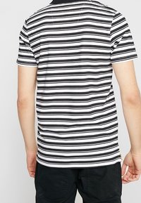 Musta-valkoraidallinen lyhythihainen poolopaita, jossa on musta yhtenäinen kaulus ja pieni logoväritys sivusaumassa. Materiaali on puuvillaa.