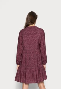 Långärmad, vinröd klänning med blommönster, med en lager-på-lager kjol och rund halsringning. Tillverkad av lätt tyg, med en avslappnad passform.