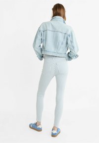 Jasnoniebieska kurtka dżinsowa o skróconym kroju, zestawiona z jasnoniebieskimi i białymi, prążkowanymi rurkami oraz niebieskimi trampkami z brązowymi podeszwami.