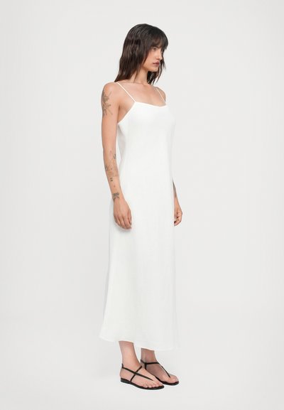 Vestido maxi blanco sin mangas con tirantes finos, corte recto, textura suave y silueta de largo completo, combinado con sandalias planas negras.