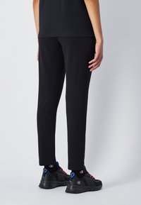 Zwarte sweatpants in een tapered ontwerp met een zachte textuur. Gecombineerd met zwarte sneakers met rode en blauwe accenten. Minimalistische esthetiek.