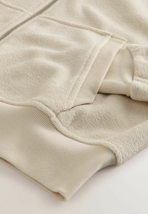 Beige fleece hoodie with ribbed cuffs and hem, featuring a soft texture and contrasting smooth zipper. Layers of fabric create dimension.
