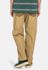 Pantalon en coton beige à coupe ample avec de grandes poches arrière, associé à un haut vert à motifs géométriques et des baskets vertes.