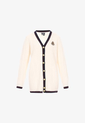 Tej-nekű krémszínű kardigán V-nyakkal, sötétkék díszítéssel, arany gombokkal, és díszítő jelvénnyel a bal mellrészen. Hosszú ujjú, bordás mandzsettával.