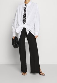 Vit oversized skjorta med knut framtill, svart mönstrad slips, svarta vida byxor och svart handväska, kompletterad med svarta sandaler.