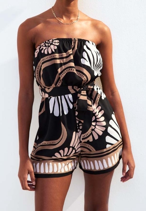 Femme portant une combinaison noire bustier avec des motifs floraux et abstraits beige et blanc, nouée à la taille avec une ceinture en tissu assortie.
