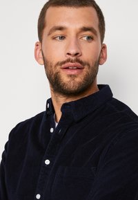 Mörkblå kord skjorta med knäppkrage, en bröstficka och diskret textur. Har vita knappar och regular fit.