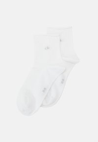 Chaussettes blanches en coton de type crew avec une texture côtelée et un petit logo "ck" gris sur le côté. Bout arrondi et bord élastiqué pour un bon ajustement.