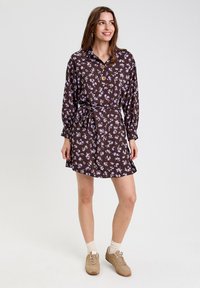 Robe fleurie brune avec un col, manches longues, boutonnière à l'avant et taille ceinturée. Le tissu a une texture douce avec de petites fleurs violettes.