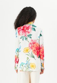 Blusa floreale bianca con grandi peonie rosa e rosse, accentuata da fiori gialli, blu e verdi. Maniche lunghe e vestibilità comoda.