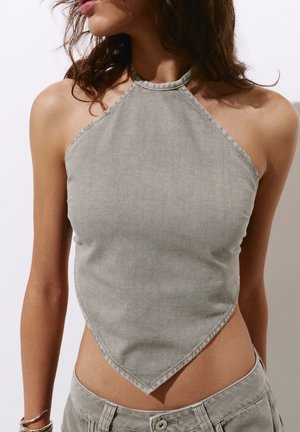 Femme portant un haut gris sans manches à col halter avec un ourlet pointu, assorti à un pantalon taille basse, laissant apparaître épaules et ventre.