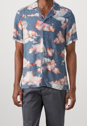 Chemise bleue à manches courtes avec boutonnière, présentant des chevaux Pégase blancs volants et des nuages roses sur fond de ciel étoilé.