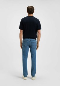 Camicia a maniche corte navy abbinata a jeans a gamba dritta di colore blu chiaro, con tasche classiche e dettagli di cuciture sottili. Indossata con scarpe chiare.