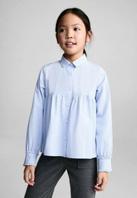 Hellblau gestreiftes langärmliges Hemd mit Button-down-Kragen und gerafftem Bund, kombiniert mit dunkelgrauen Hosen. Vorderansicht, lockere Passform.