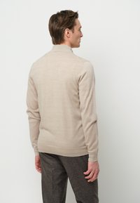 Suéter de punto beige con mangas largas y un cuello alto, mostrado desde la parte de atrás. Tejido texturizado con un acabado suave.
