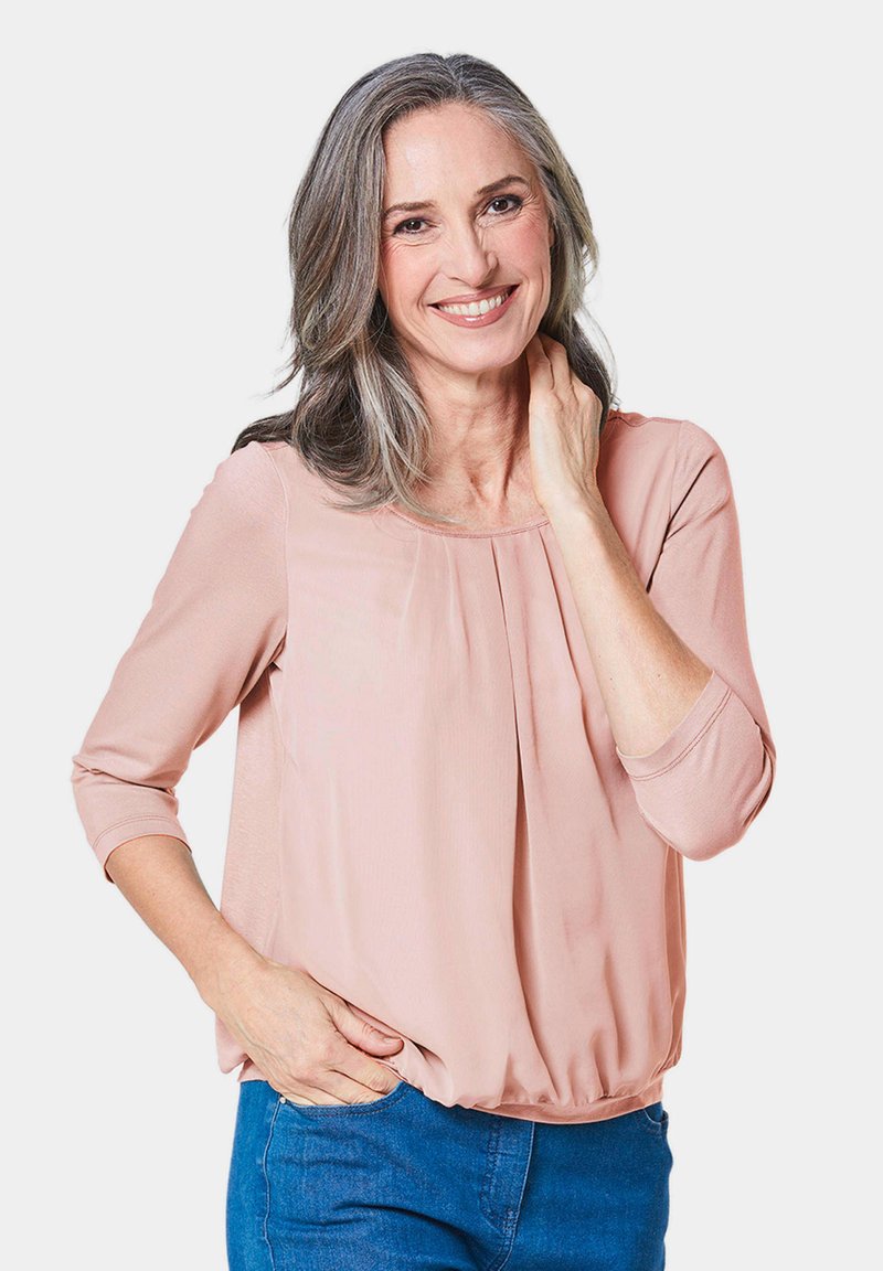 Blush-pink, leichtes Blusenshirt mit Dreiviertelärmeln, rundem Ausschnitt und gerafftem Bund. Kombiniert mit blauen Jeans.