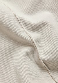 Tissu beige clair avec une fine texture côtelée et une couture courbée traversant la surface en diagonale.