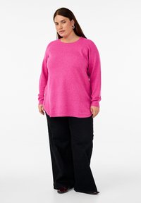 Pink oversized sweater with long sleeves and a rounded neckline, paired with black wide-leg pants. Sweater has a soft, textured finish.