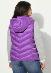 Gilet imbottito viola con cuciture a zigzag, cappuccio e maniche grigie. Presenta una trama lucida, polsini a contrasto e una vestibilità comoda.