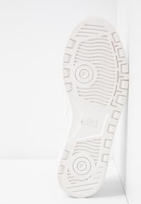 Weiße Sportschuhsohle mit einem strukturierten Gummi-Griffmuster, kreisförmigen und linearen Designs sowie dem eingeprägten "asics"-Logo.