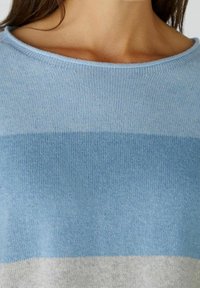 Jasnoniebieski sweter z poziomymi paskami w różnych odcieniach niebieskiego oraz jasnoszarym pasem na dole. Miękki dzianinowy materiał i szeroki dekolt.