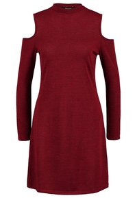 Abito rosso a maglia con maniche lunghe e spalle scoperte, caratterizzato da un colletto alto e una vestibilità rilassata. Tessuto morbido, lunghezza al ginocchio.