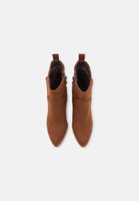Bottines en daim marron avec un bout pointu, dotées d'une fermeture éclair sur le côté extérieur et d'une petite languette à l'arrière.