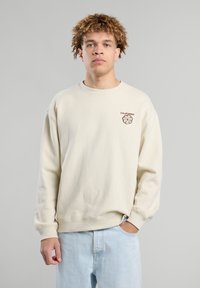 Sudadera de color beige claro, material de algodón, con cuello redondo, puños y dobladillo de canalé, que presenta el texto 'CALIFORNIA' y un diseño de flores en marrón.